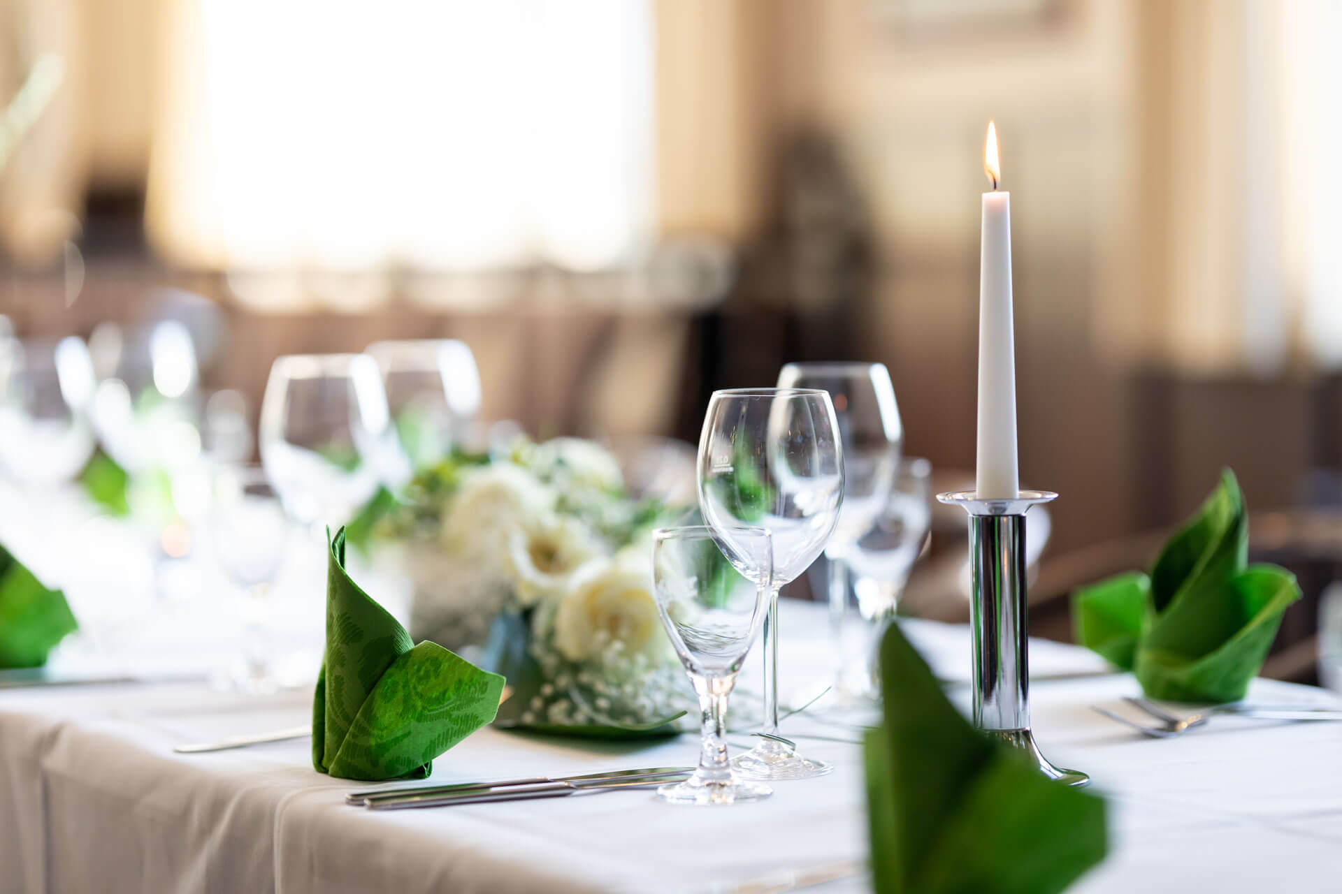 Gedeckter Tisch im Restaurant L&uuml;bsche Thorweide mit Gl&auml;sern, gr&uuml;nen Servietten und einer brennenden Kerze